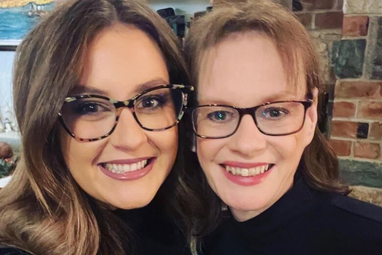 Two women in glasses and black shirts smile at the camera.