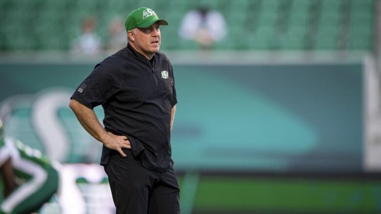 Football coach stands on sideline with hands on his hips.