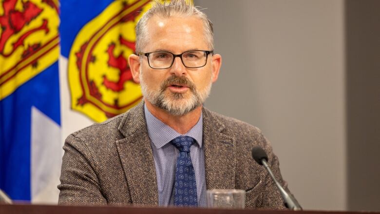 A man with glasses and a beard smiles while listening to questions.