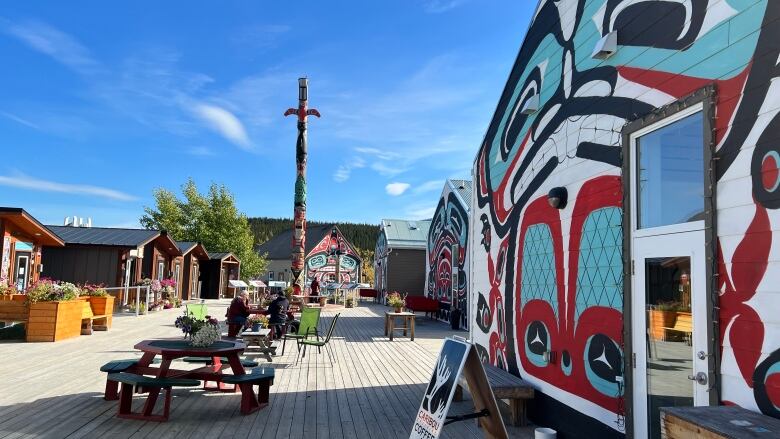 Cabins covered in Indigenous art, picnic tables, a sign inviting people to buy coffee. 