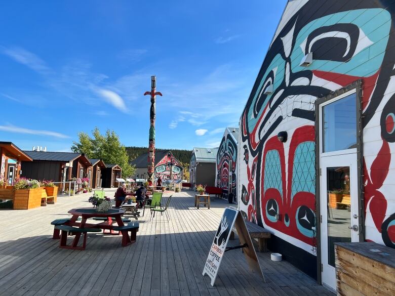 Cabins covered in Indigenous art, picnic tables, a sign inviting people to buy coffee. 