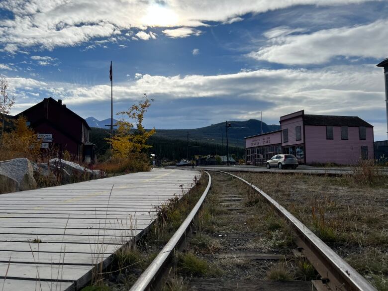 Railway tracks in dirt, a wooden walkway, pointing to a colourful town.