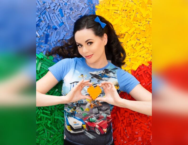 A woman holds a heart made of yellow Lego bricks, with Lego bricks in blue, yellow, green and red in the background.