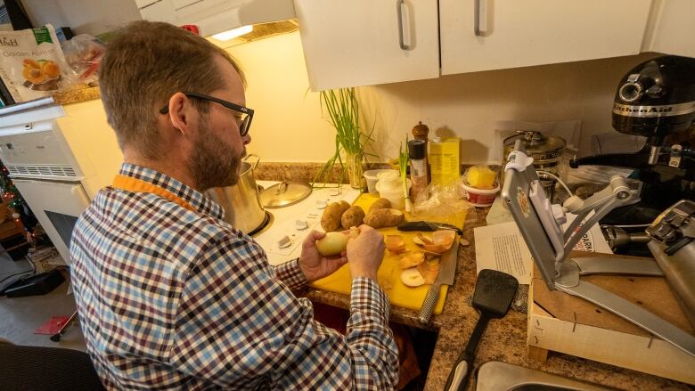 A man in a wheelchair peels potatoes by a kitchen counter, and an iPad is nearby facing the counter.