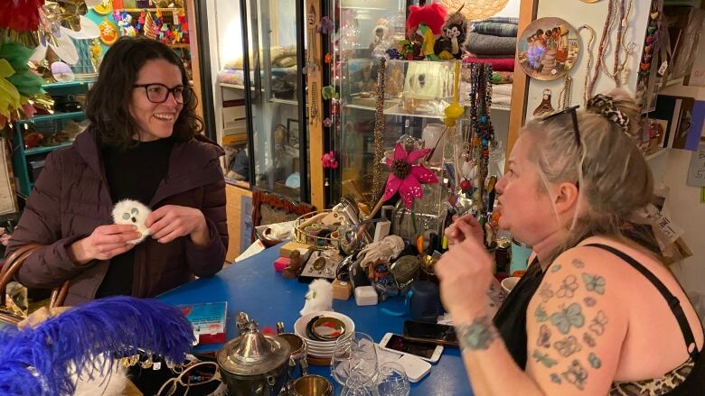 Woman talking to another woman in cluttered, colourful retail store.