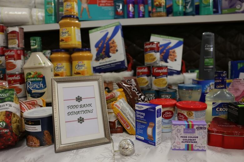 Canned goods, pantry items and toiletries are stacked on a table with a framed photo that says 