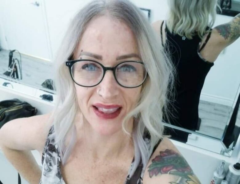 A woman with tattoos and black-rimmed glasses takes a selfie