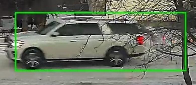 A still surveillance photo shows a white SUV driving on a snow-packed road. The vehicle is framed by a green rectangle. 