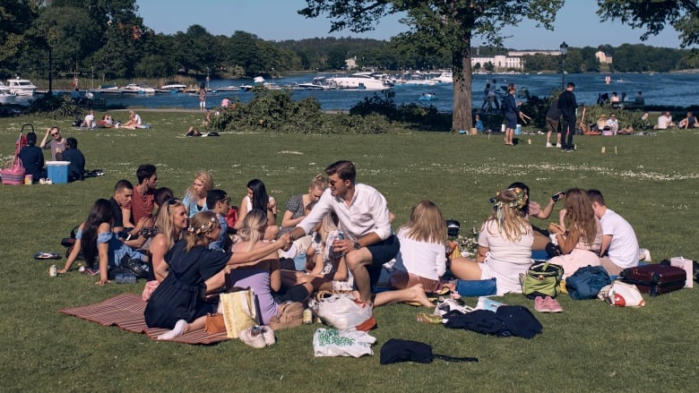 Swedish people celebrate Midsummer celebration in Stockholm in June 2020. They are picnicking in a park. 