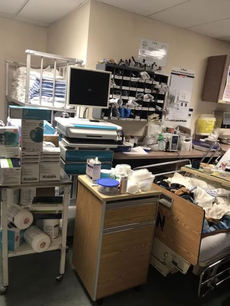 A patient in a hospital bed in a cramped, cluttered storage room.