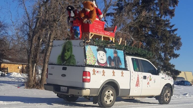 A truck with a Santa sleigh on the roof and holiday designs covering its exterior drives through the snow.