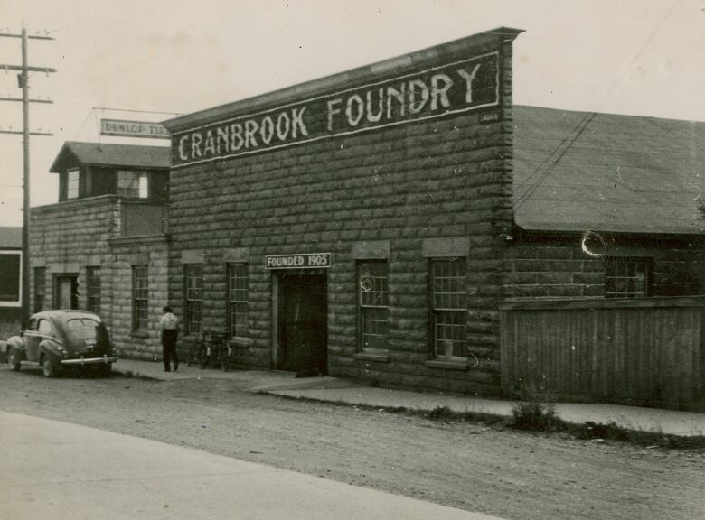 A building made of bricks stands on the street, with a person and a car in front of it.