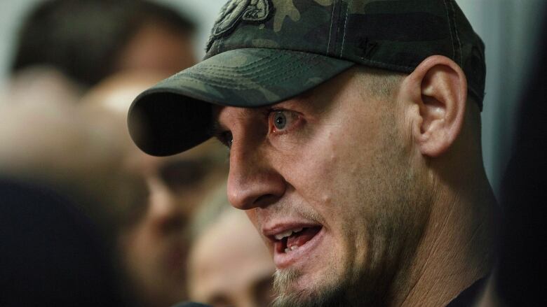 A man wearing a hat is seen giving an interview to reporters.