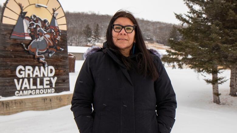 A woman stands in the snow wearing a big winter jacket and glasses.