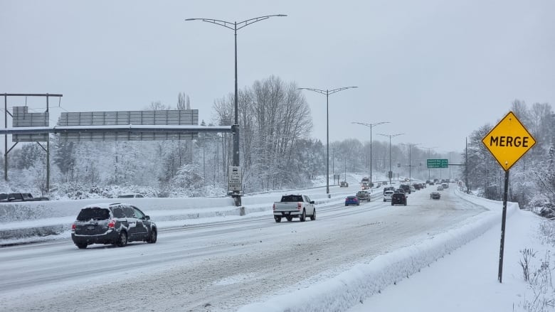 A row of vehicles on a snowy highway, with the guard rails covered by snow.