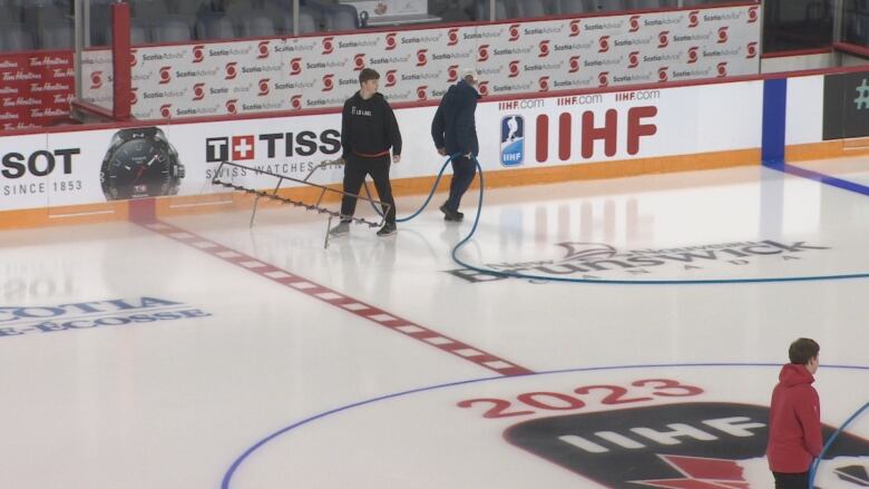 A team of men are walking on the ice with a hose spraying water as they rebuild the ice surface at Scotiabank Centre in Halifax for the competition.