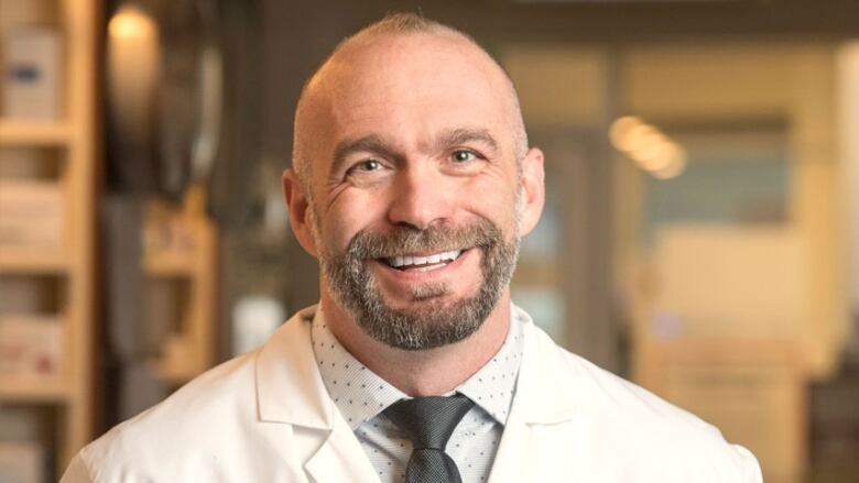 A portrait of a smiling man wearing a white lab coat.