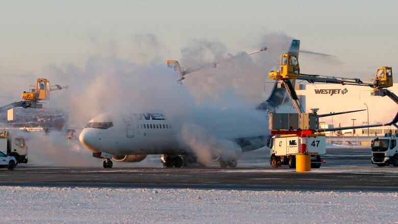 Clouds of steam rise from a white airplane positioned on a runway marked with snow. 