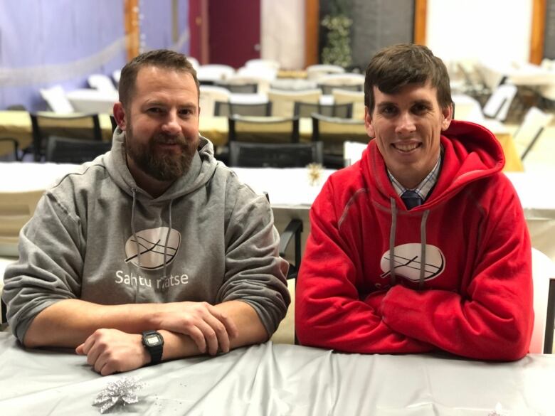 Two men sitting at a table smile at the camera.