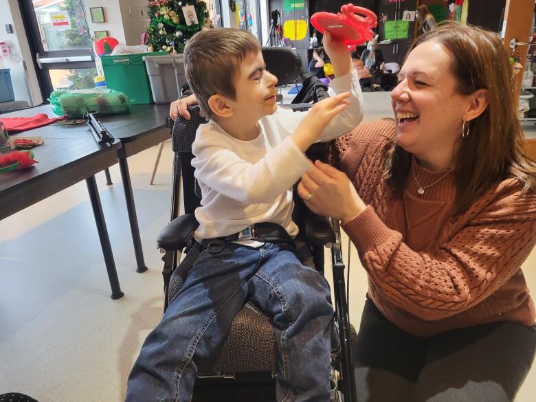 A boy in a wheelchair and a woman crouching down beside him, smiling. 