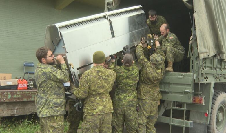 Soldiers lifting something big into a truck 