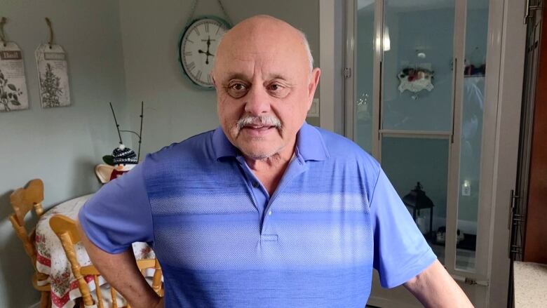 A middle-aged white man stands in a kitchen in a purple polo shirt.