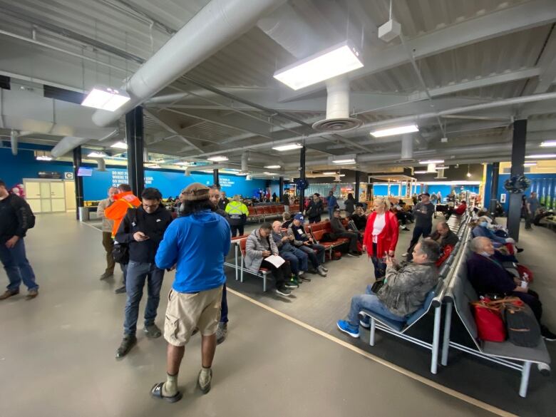 A crowd of people are standing and sitting in an airport terminal.