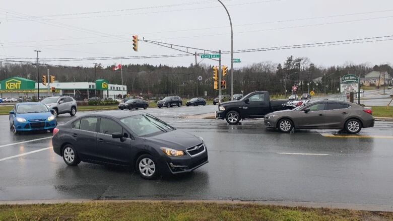 A black car drives along a rainy street, surrounded by other cars in a busy intersection.