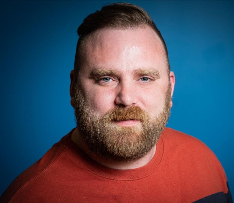 A headshot of a man in an orange shirt standing against a blue background.