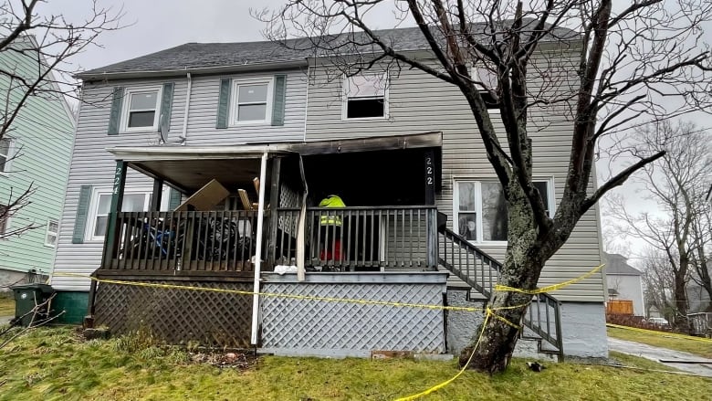 The front of a duplex is shown with the front porch blackened from fire and yellow police tape stretched across the lawn.