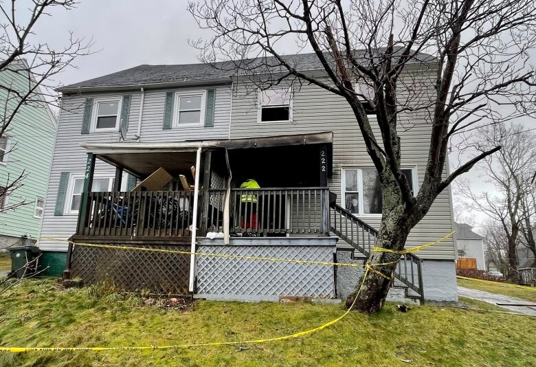 The front of a duplex is shown with the front porch blackened from fire and yellow police tape stretched across the lawn.