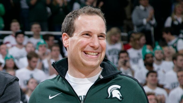 Mat Isbia smiles as he wears a green Michigan State quarter-zip on the court in front of a crowd full of cheering fans.