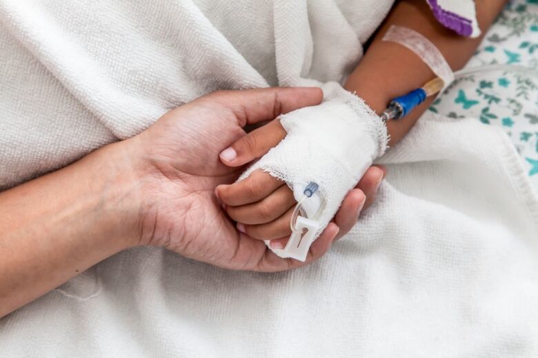 A mother holds a child's hand in the hospital. The child is connected to an IV