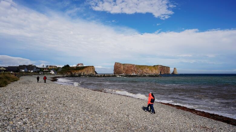 People walk along the beach with Perc Rock