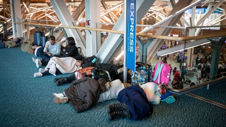 People lie on the ground with jackets covering them as they try to sleep.