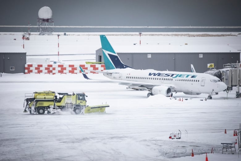 A Westjet plane sits in the snow as a plow drives by.