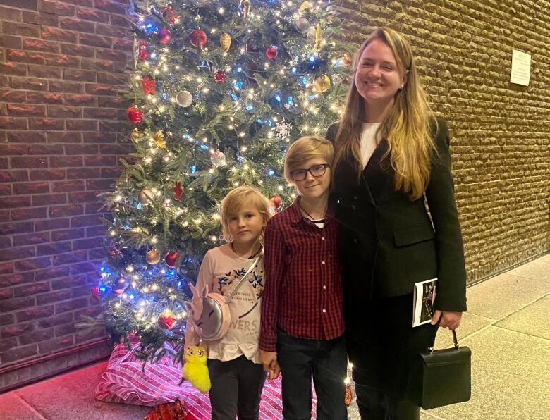 A mother and her two kids stand in front of a Christmas tree.