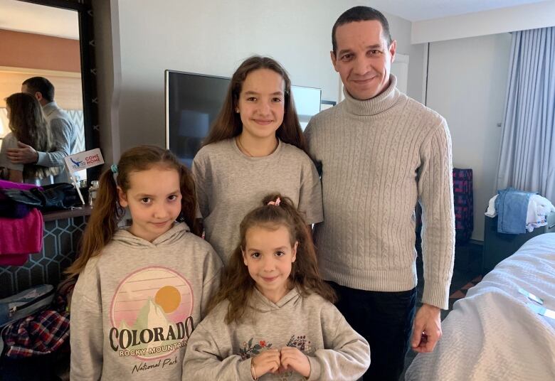 Three girls and their father smile for a picture in a hotel room.