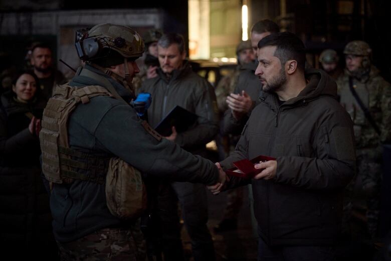 The Ukraine president, dressed in green army fatigues, shakes hands with a uniformed soldier.