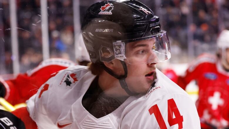 A hockey player wearing a black helmet and a white jersey. Number 14 is on the shoulder. 