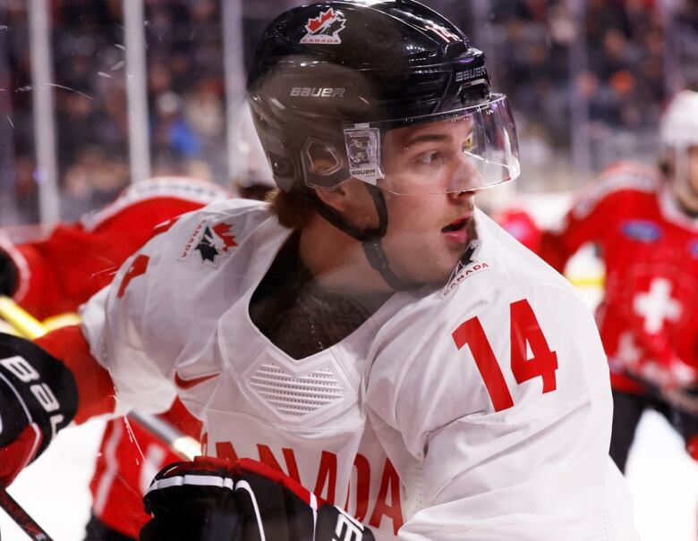 A hockey player wearing a black helmet and a white jersey. Number 14 is on the shoulder. 