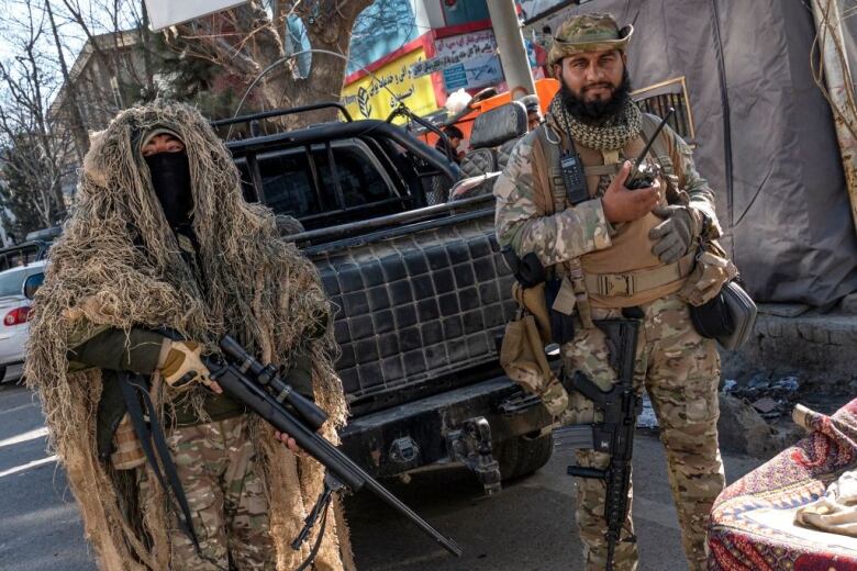 Two Taliban security personnel stand guard along a road in Kabul.