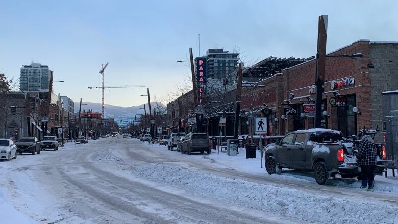 A road with plowed snow and cars and shops on both sides.