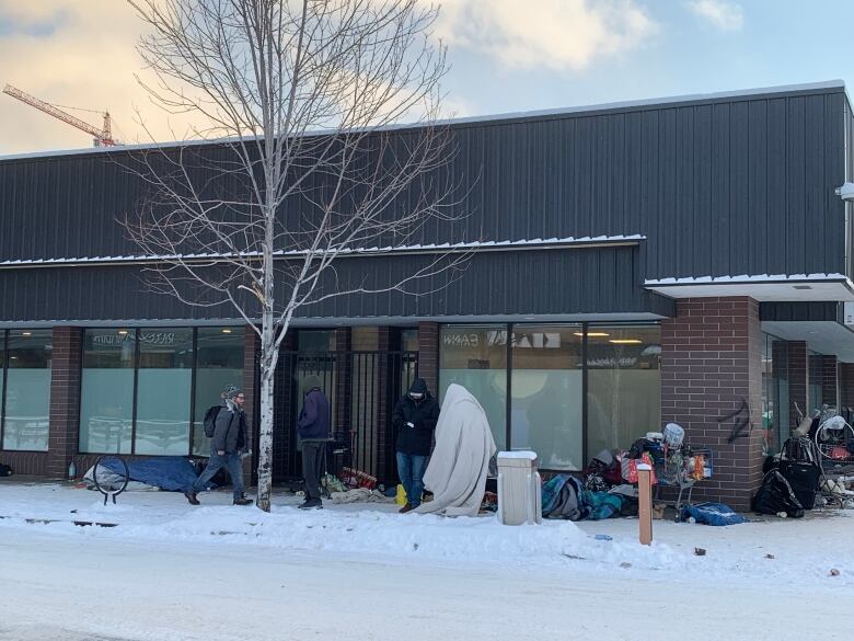 A group of people gather near a building with glass windows, with snow on the road in front of it.