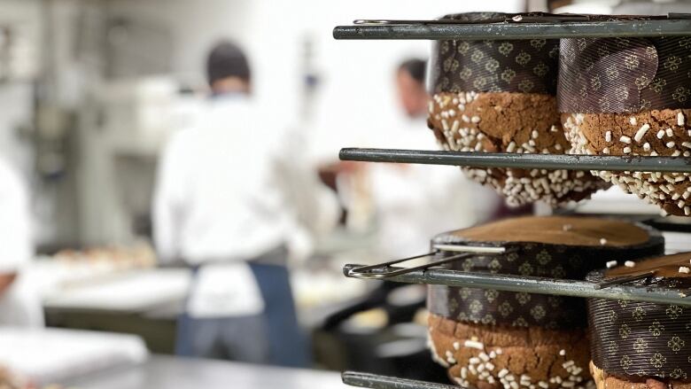 Panettone sweet breads hang in rows from rack in pastry kitchen as chefs work in background