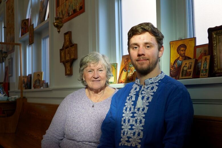 An elderly woman sits beside a young man in a Ukrainian Orthodox church.