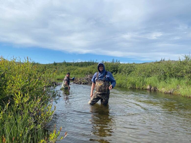 Two people wade through a river that comes up just past their knees.