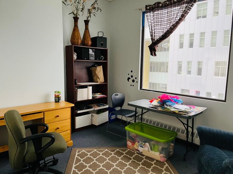 A large, bright room with desks, chairs, and a bookshelf overlooking an office building in downtown Yellowknife.