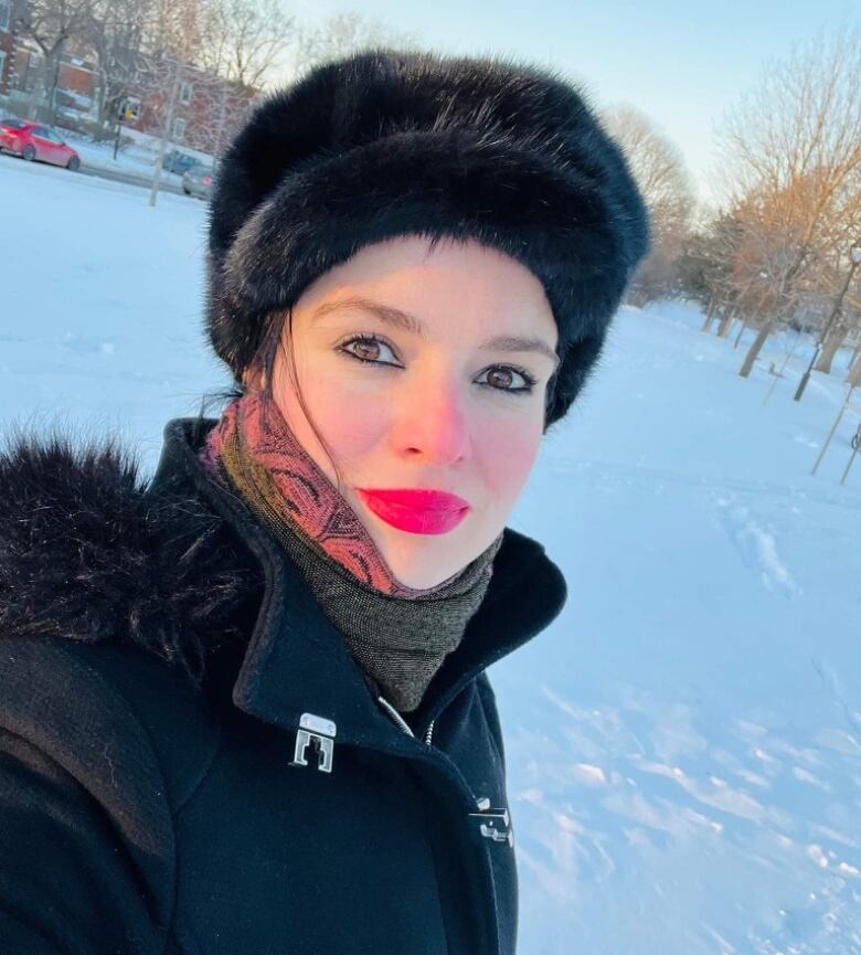 A fashionable woman wearing a fur hat is bundled up against the cold in a winter time portrait.