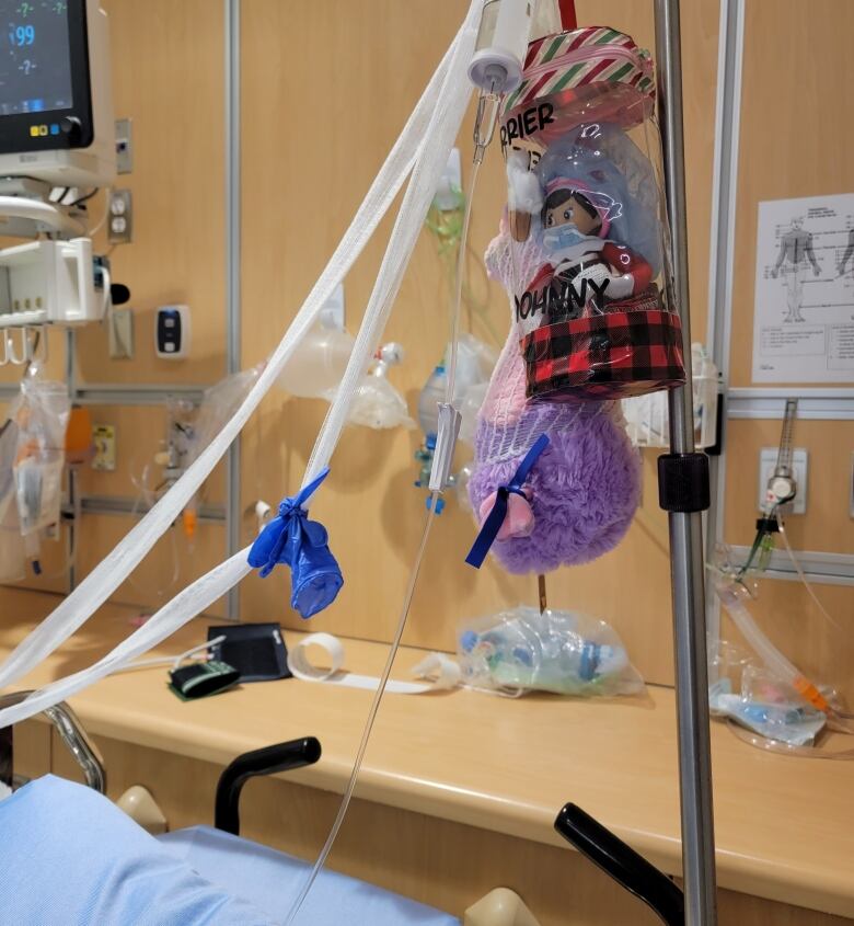 An Elf on the Shelf hangs in a clear plastic bag beside a hospital bed.